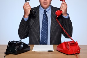 Businessman sat at desk with two telephones.